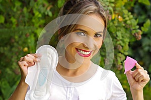 Close up of a young smiling beautiful woman holding a menstrual cup in one hand and a hygienic towel in her other hand