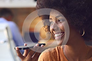 Close Up Of Young Smiling Businesswoman Working At Desk In Office Talking Into Mic Of Mobile Phone