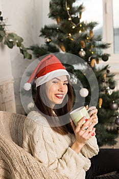 Close up of a young smiling girl holding a green cup of cacao near Christmas festive tree
