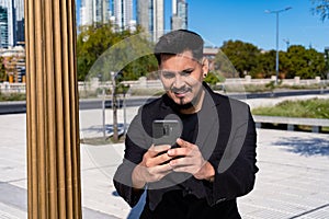 Close-up of young smiling Latino checking and answering messages with his cell phone or smart phone in a public square. Concept