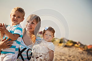 Close up of young smiling mother hugging her small kids, having fun at beach together, happy lifestyle family concept