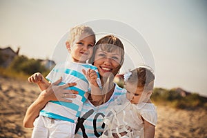 Close up of young smiling mother hugging her small kids, having fun at beach together, happy lifestyle family concept.