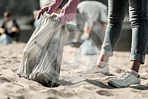 Close up of young student wearing jeans and sneakers cleaning up trash on the beach