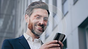 Close-up young surprised man looks at phone screen receiving notification reading good news rejoicing in success