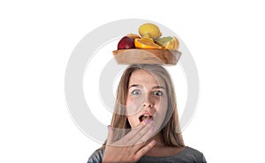 Close up of young surprised woman which is holding a wooden bowl with fruits: apples, oranges, lemon. Vitamins and healthy eating.