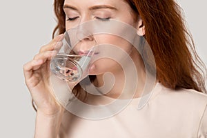 Close up young thirsty red-headed woman drinking clean water