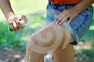 Close-up of young woman applying insect repellent onto leg in park