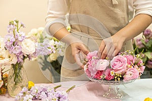 Close up of young woman arranging beautiful pink rose flower bouquet vase on table