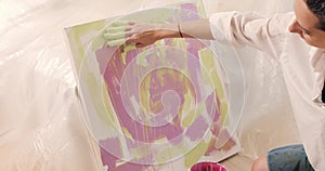 Close-up of young woman artist in a white shirt painting picture by hands in art studio.