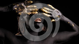 Close-up of a young woman with black and gold paint on her skin posing in Studio