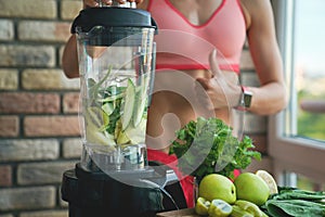 Close up of young woman with blender and green vegetables making detox shake or smoothie at home