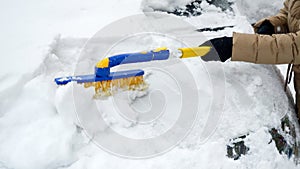 Close-up of a young woman brushing snow from her car on a snowy day. Concept of winter, car care, and daily chores