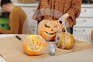 Close up of young woman carving Jack O Lattern from ripe orange pumpkin with knife on her wooden kitchen table. Female