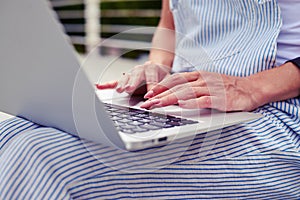 Close-up of young woman in casual clothes typing on laptop outd