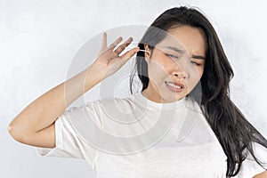 Close up young woman cleaning ears, using cotton bud after shower, feeling pain, beautiful female wearing white t-shirt standing