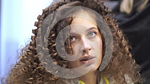Close-up of a young woman with curly hair who is getting her hair done, she is talking while looking at the camera