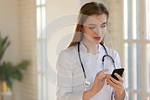 Close up young woman doctor using smartphone, standing in office