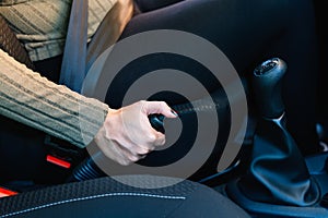 Close-up of a young woman driver's hand using the handbrake of her car.