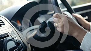 Close up of Young woman driving a car, hand put on the black steering wheel and looking forward with determination.