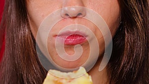 Close-up of a young woman eating a slice of pizza. The girl bites off the fast food with her teeth