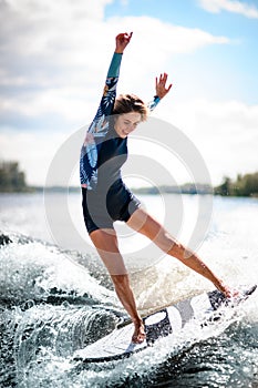 Close-up of young woman elegantly balances on surfboard riding the wave.