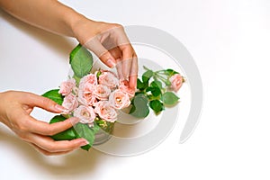 Close up of young woman florist hand creating bouquet of pink roses on a light