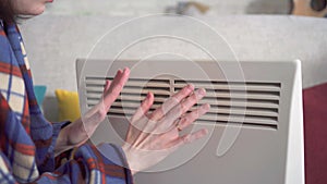 Close up young woman freezes in the living room and heats herself next to an electric heater