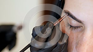 close up. young woman gets eyebrow correction procedure. kosmetolog- makeup artist applies paint with brush on eyebrows