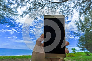 Close up young woman hand holding a modern black smartphone mock up in horizontal position with blank screen against beautiful blu