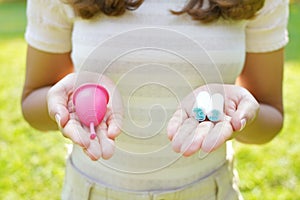 Close-up of young woman hands showing collector menstrual cup and tampons