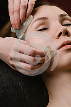 Close up of a young woman having a gua sha face massage at asian beauty clinic