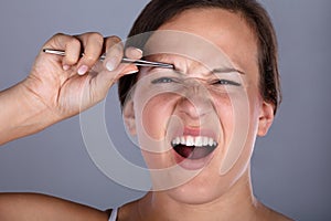 Woman Having Pain While Plucking Eyebrow Hair With Tweezers