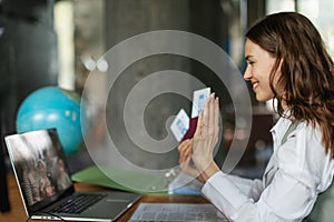 Close up of young woman holding plane tickets, having online call.