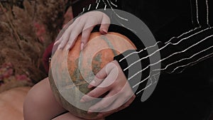 Close-up of a young woman holding a pumpkin in a Park with autumn fallen leaves.