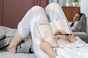 Close-up of a young woman in home pajamas lying in bed and making a wish list. concept of planning, goals, future,