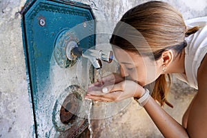 Close up of young woman hydrates herself from a fountain during a heat wave in the city photo