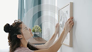 Close-up of young woman interior designer hanging modern picture on wall indoors in apartment