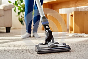 Close up of young woman in jeans cleaning carpet with vacuum cleaner in living room, copy space. Housework, household.