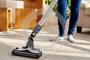 Close up of young woman in jeans cleaning carpet with vacuum cleaner in living room, copy space. Housework, household.