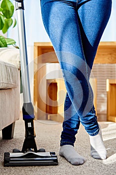 Close up of young woman in jeans cleaning carpet with vacuum cleaner in living room, copy space. Housework, household.