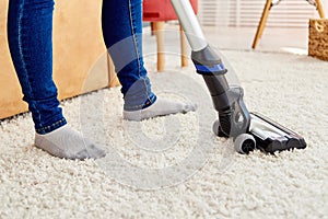 Close up of young woman in jeans cleaning carpet with vacuum cleaner in living room, copy space. Housework, household.