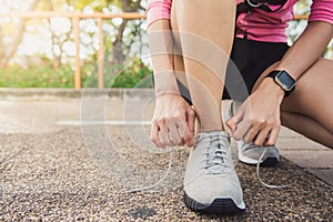 Close up of young woman lace up her shoe ready to workout on exercising in the park with warm light sunshine in morning.