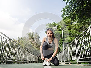 Close up of young woman lace up her shoe ready to workout on exercising in the park with warm light sunshine in morning.