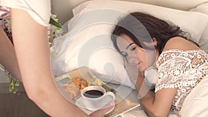 Close-up of young woman lying asleep and her tender husband coming to her with breakfast