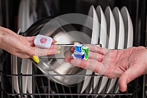 Close-up of young woman and man hands holding two colored capsule for the dishwasher. In the background, out of focus, is a