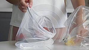 Close up of young woman move vegetables from plastic bag to reusable mesh bag on the kitchen wooden table. Zero waste