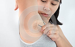 Close up of young woman plucking armpit underarm with tweezers  on grey background. Concept of Hygiene skin body care and