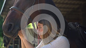 Close up of young woman preparing her horse, putting bridle and harness. Woman fixing mane from harness in a riding