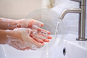 A close up of a young woman`s hand washing hands with soap gel in the bathroom sink hand cleaning to prevent the spread of the