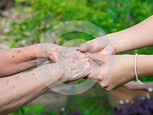 Close-up of a young woman`s hands holding an elderly female`s hands. Concept of aged people and healthcare